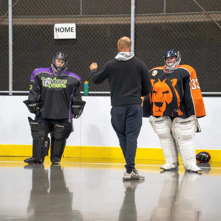 Person in lacrosse goalie gear interacting with a coach on a lacrosse floor.